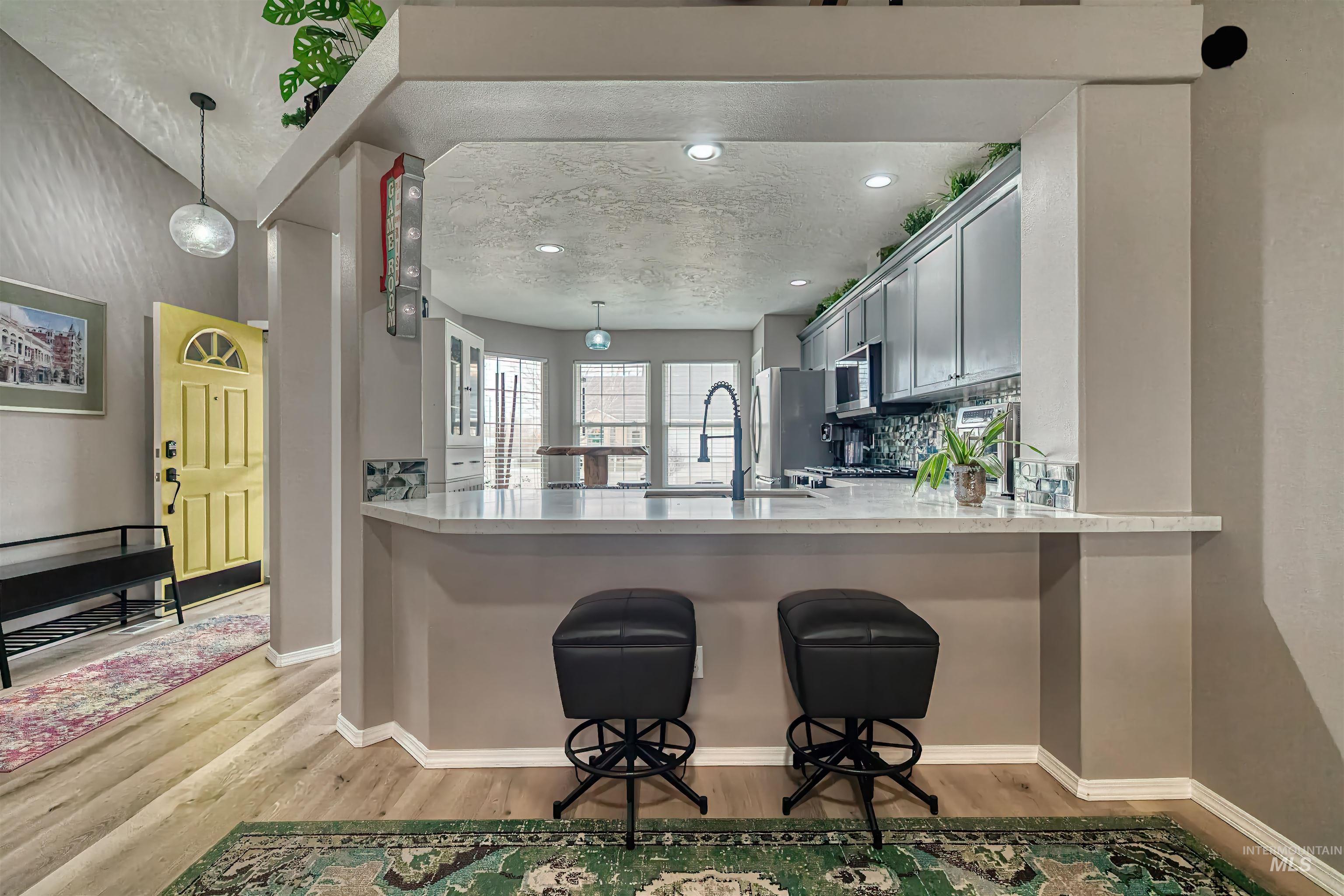 Kitchen featuring pendant lighting, a kitchen breakfast bar, backsplash, light wood finished floors, and light stone countertops