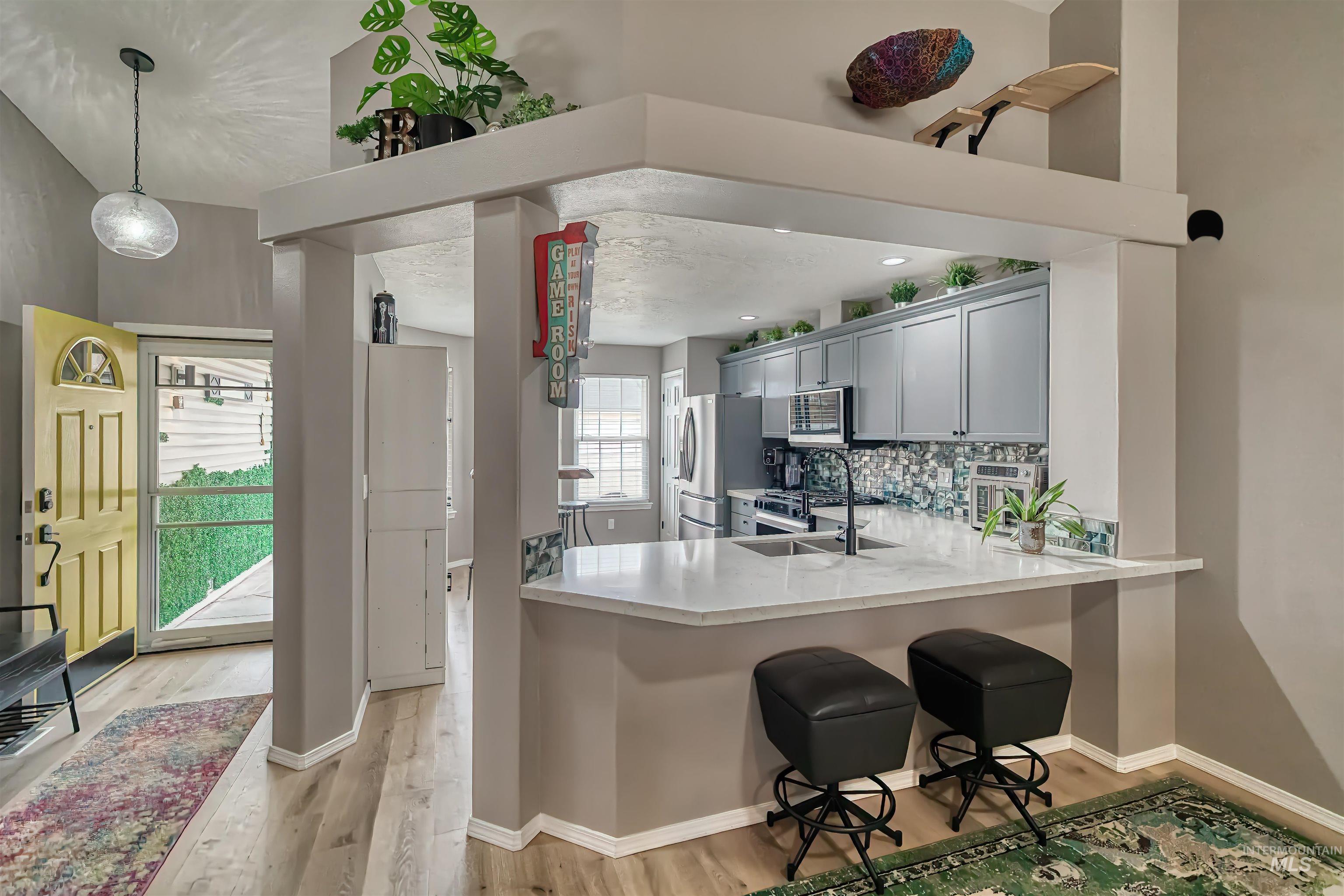 Kitchen featuring light wood-style floors, hanging light fixtures, backsplash, a breakfast bar, and gray cabinetry