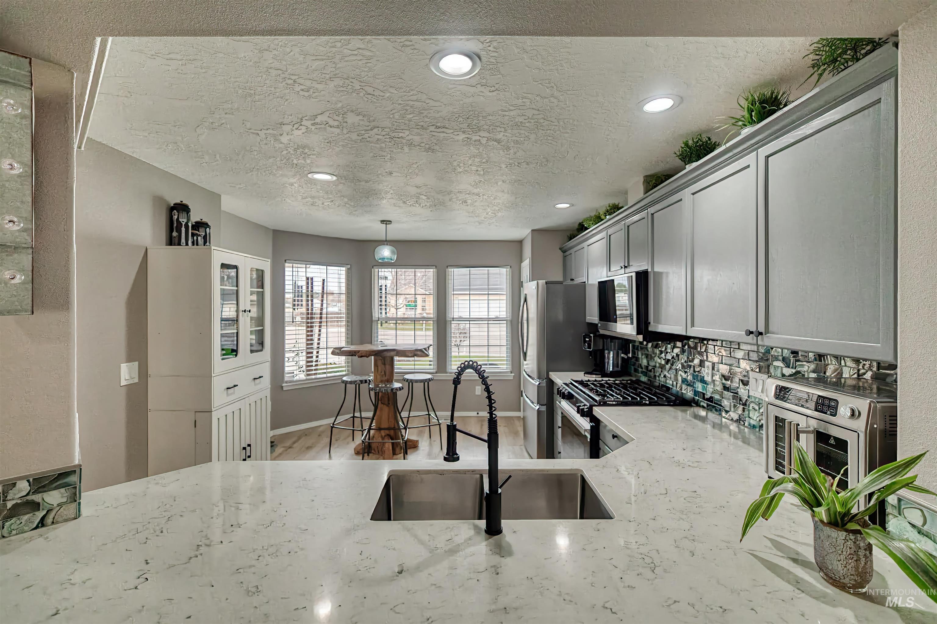 Kitchen with appliances with stainless steel finishes, a textured ceiling, decorative light fixtures, light stone counters, and backsplash
