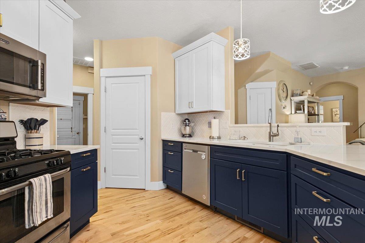 Kitchen with blue cabinets, stainless steel appliances, white cabinetry, pendant lighting, and decorative backsplash