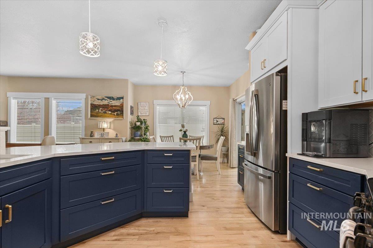 Kitchen with blue cabinetry, hanging light fixtures, stainless steel fridge with ice dispenser, light wood-type flooring, and white cabinetry