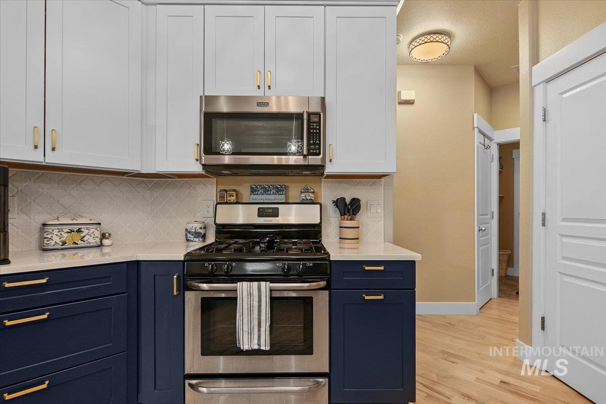 Kitchen with appliances with stainless steel finishes, tasteful backsplash, blue cabinetry, white cabinets, and light stone countertops