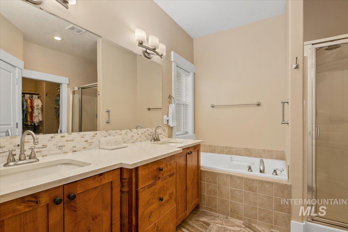 Bathroom featuring a walk in closet, a stall shower, double vanity, a bath, and tasteful backsplash