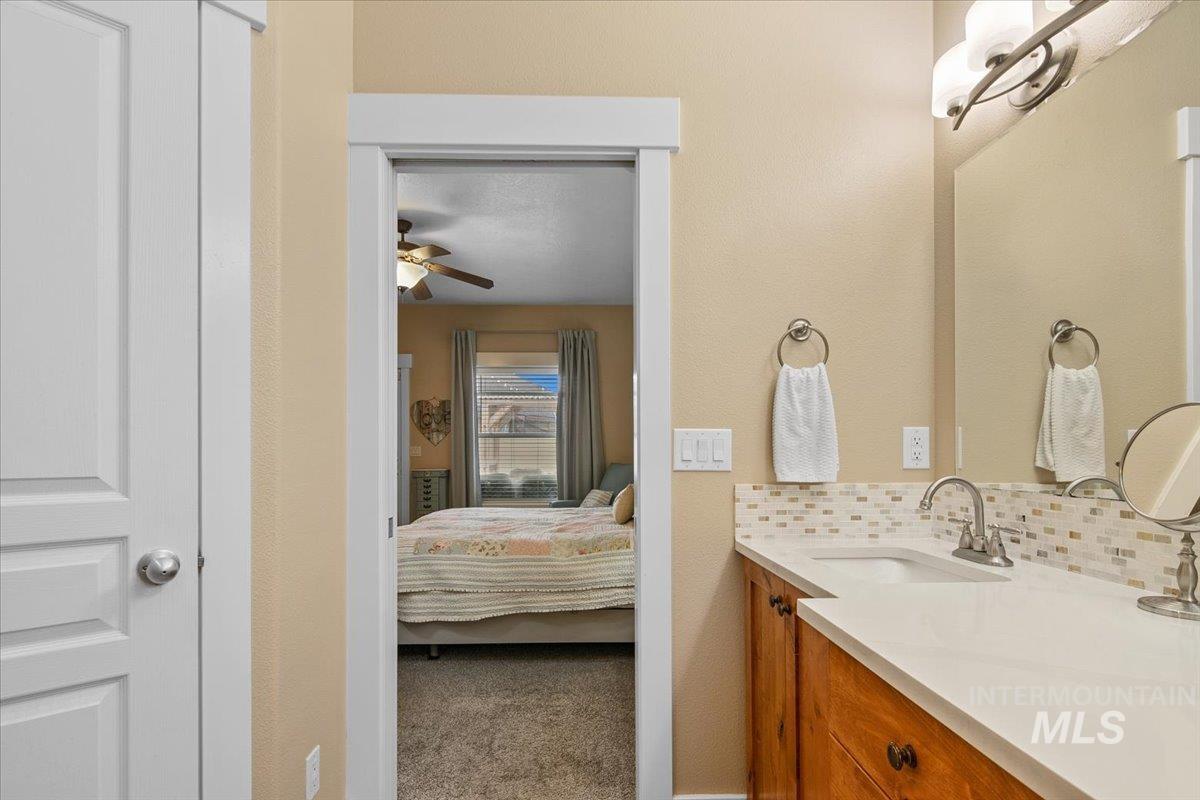 Ensuite bathroom featuring carpet, vanity, decorative backsplash, and ceiling fan