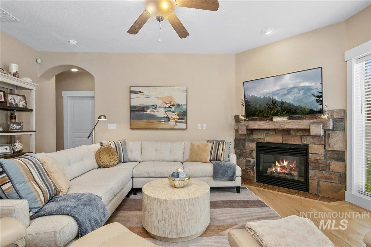 Living room with wood finished floors, a fireplace, arched walkways, and ceiling fan