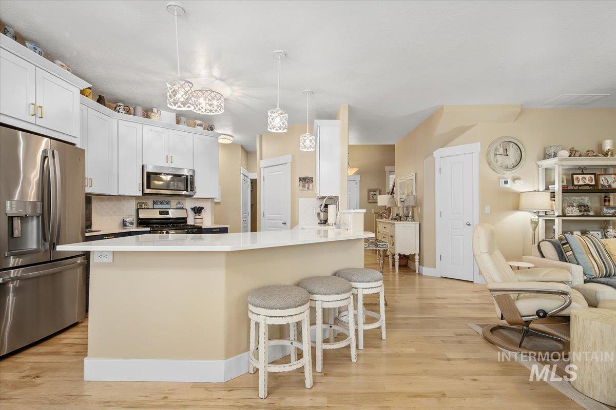 Kitchen with backsplash, a kitchen breakfast bar, appliances with stainless steel finishes, and decorative light fixtures