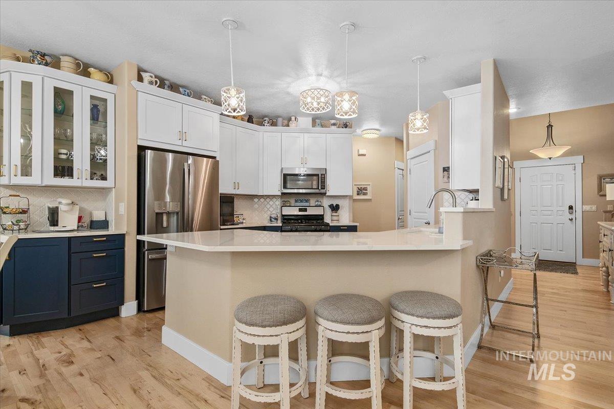 Kitchen with decorative light fixtures, backsplash, a kitchen bar, and white cabinetry