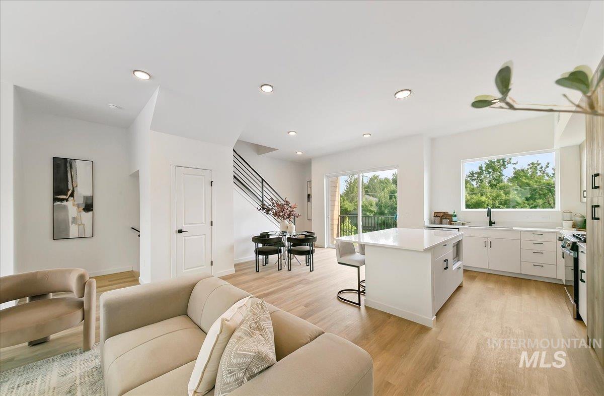 Kitchen featuring a breakfast bar area, white cabinetry, open floor plan, light wood-style flooring, and a center island