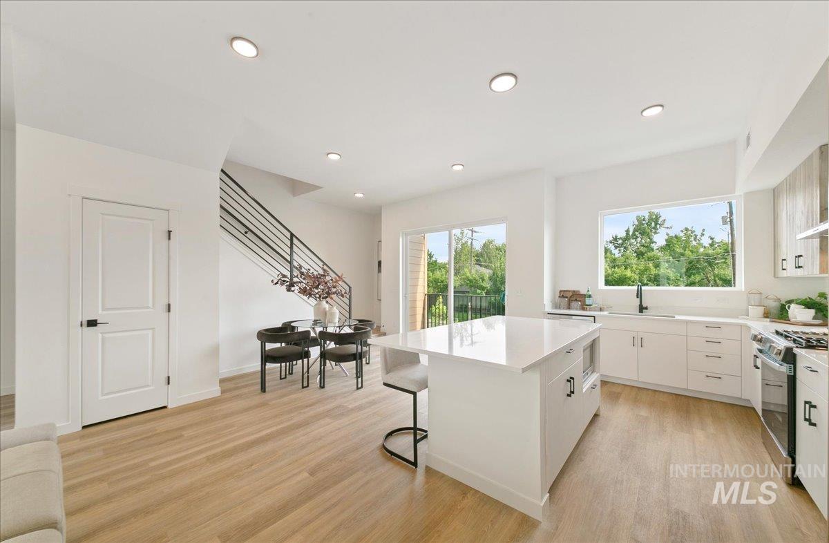 Kitchen featuring white cabinets, a breakfast bar, a center island, stainless steel gas range oven, and light wood finished floors