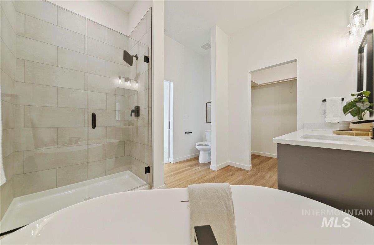 Full bathroom with a shower stall, double vanity, a soaking tub, a walk in closet, and light wood-style floors