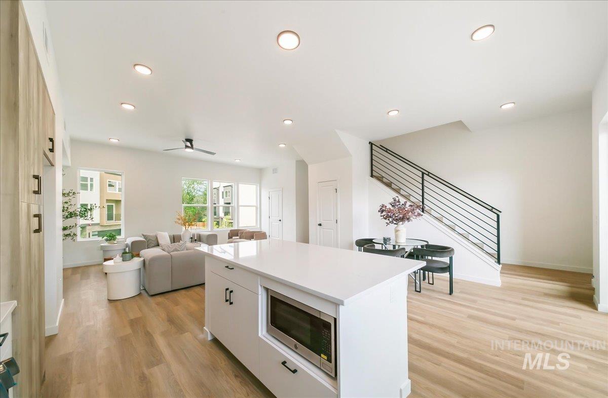 Kitchen with light wood-style flooring, recessed lighting, stainless steel microwave, a center island, and white cabinetry