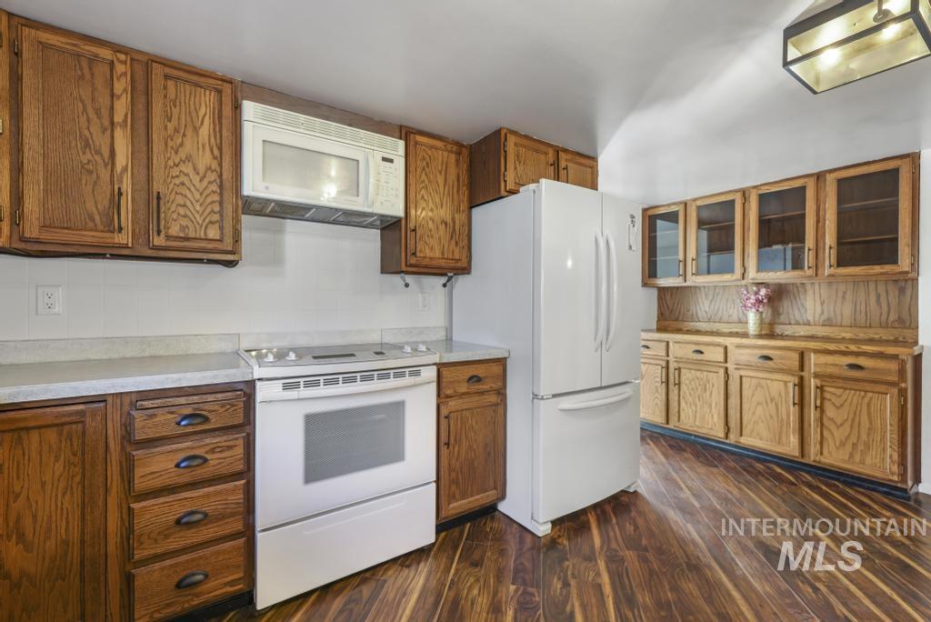 Kitchen with white appliances, brown cabinetry, light countertops, and dark wood-type flooring
