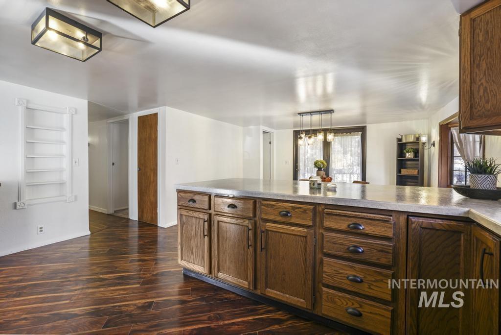 Kitchen with dark wood-style flooring, hanging light fixtures, a peninsula, built in features, and light countertops
