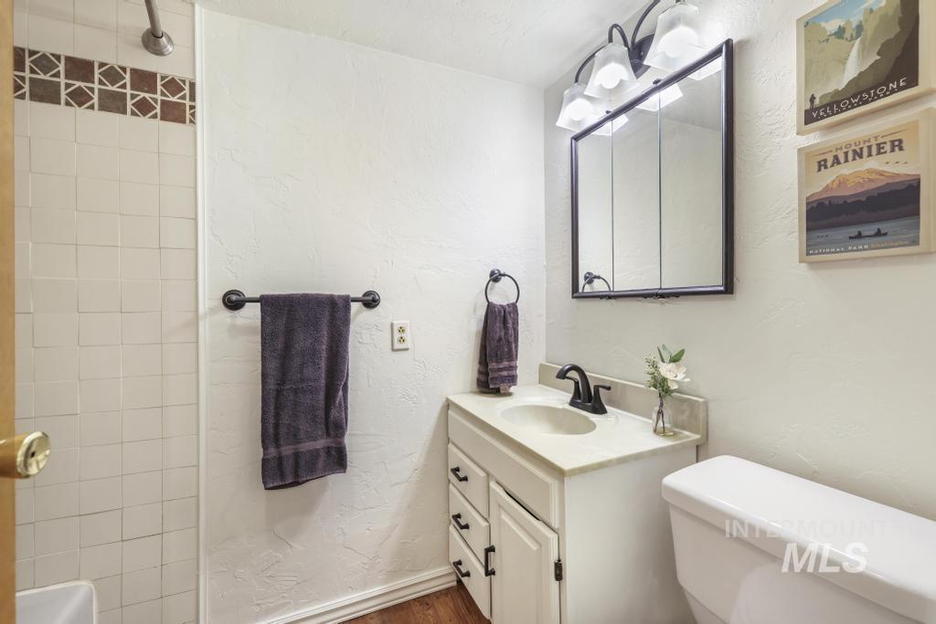 Bathroom with a textured wall, vanity, dark wood-type flooring, and a shower