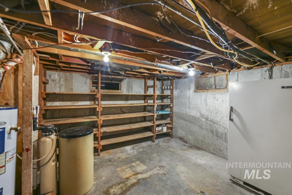 Unfinished below grade area featuring freestanding refrigerator, water heater, and a water softener system
