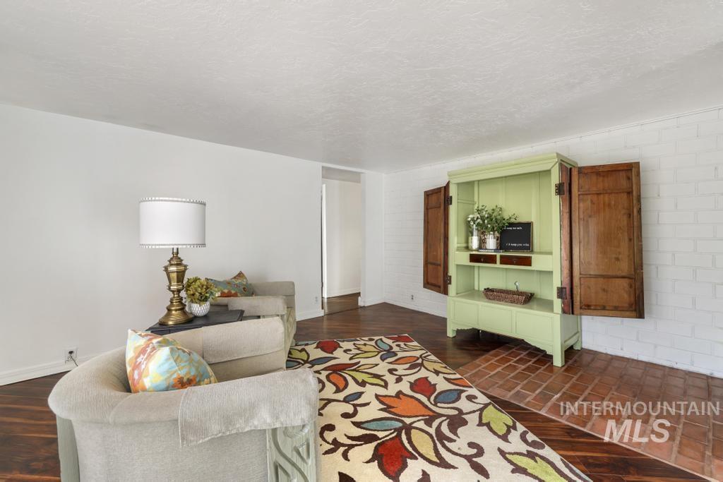 Living area featuring a textured ceiling, dark wood finished floors, and brick wall