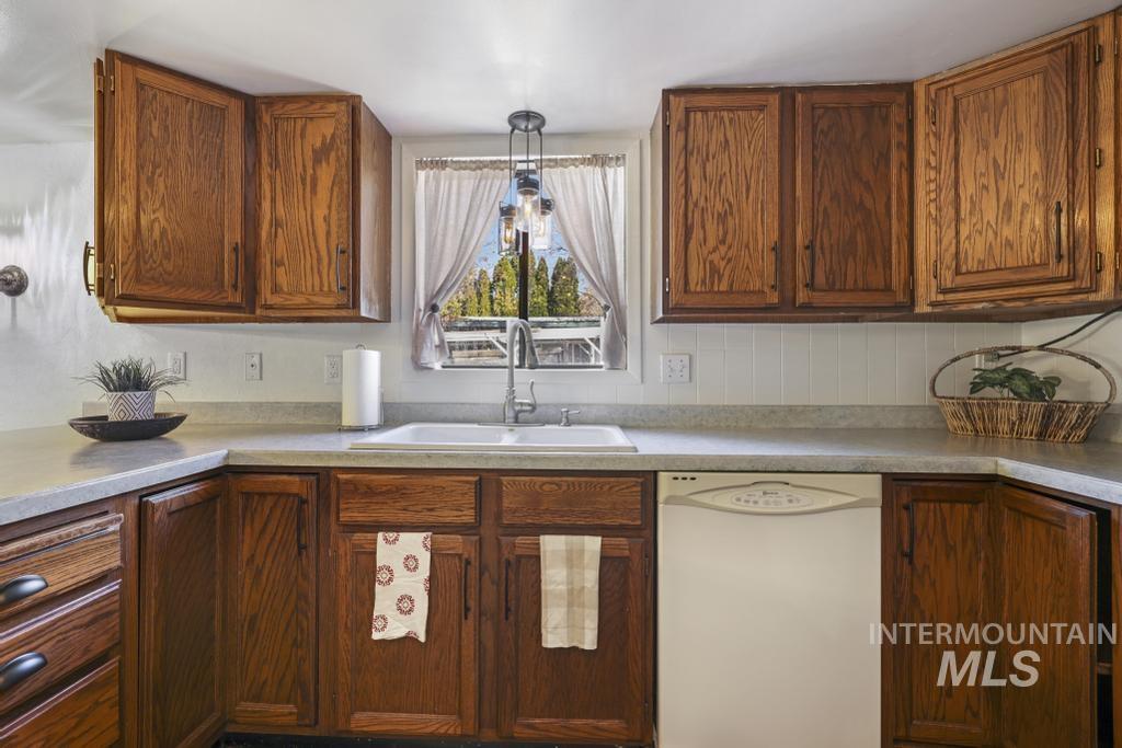 Kitchen with dishwasher, light countertops, brown cabinetry, and pendant lighting