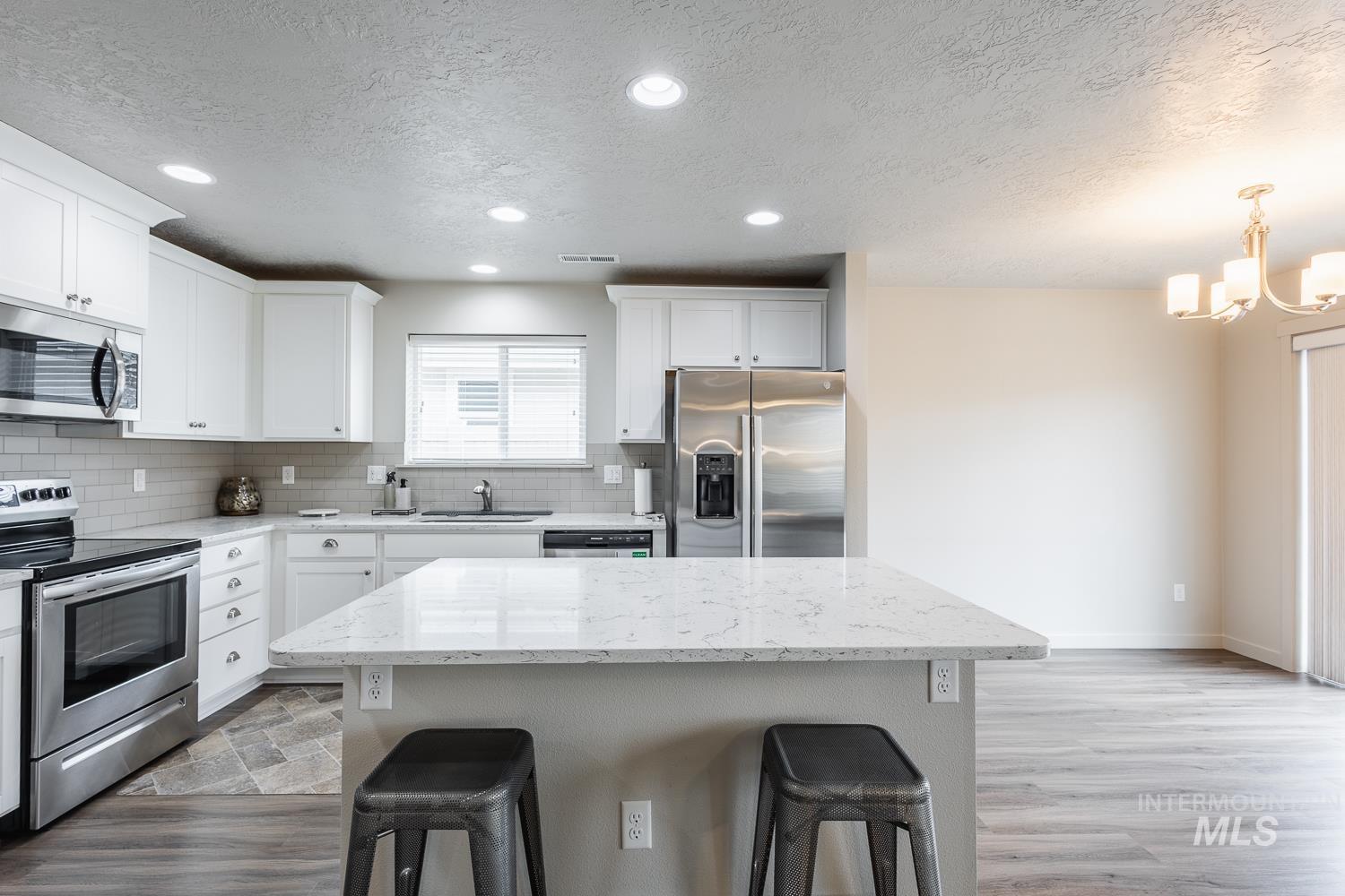 Kitchen featuring stainless steel appliances, a textured ceiling, a breakfast bar area, light stone countertops, and a kitchen island