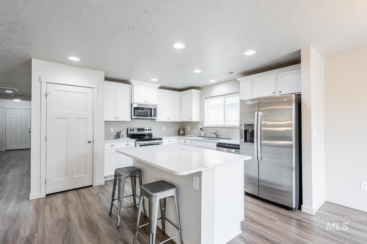 Kitchen with appliances with stainless steel finishes, light stone countertops, a breakfast bar, a textured ceiling, and a kitchen island