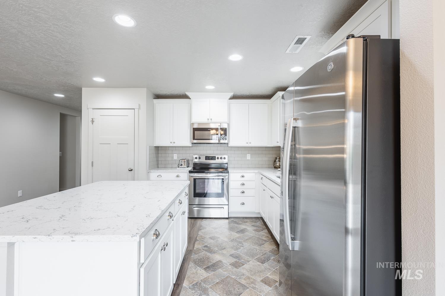 Kitchen with stainless steel appliances, white cabinetry, a center island, light stone counters, and recessed lighting