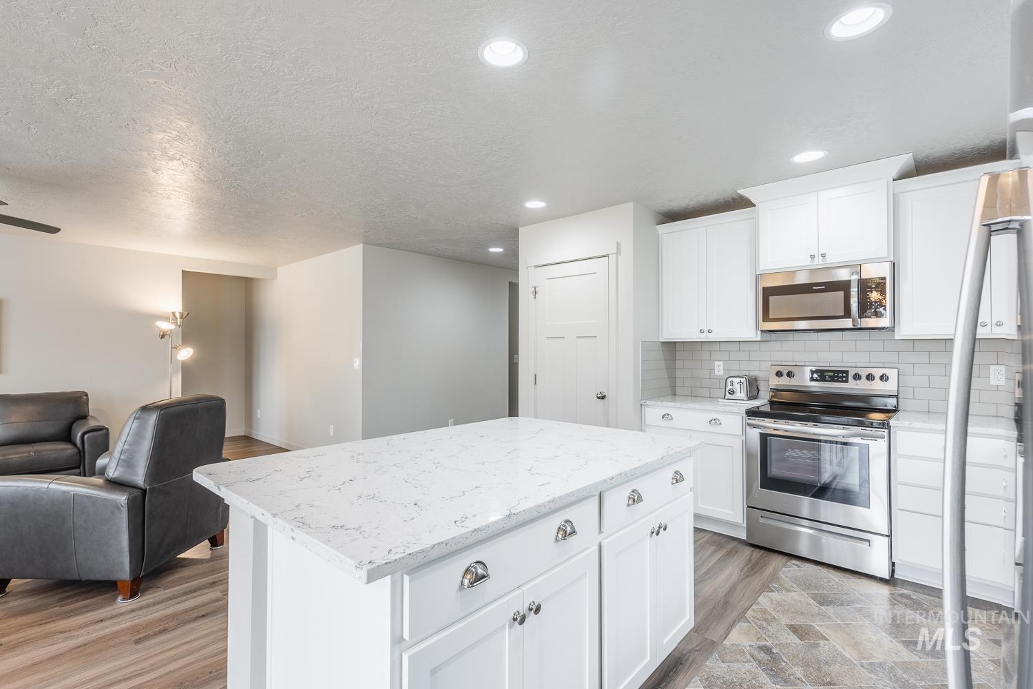 Kitchen with appliances with stainless steel finishes, open floor plan, decorative backsplash, white cabinetry, and a center island