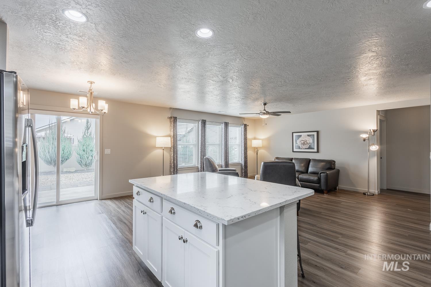 Kitchen featuring white cabinetry, light stone counters, stainless steel fridge with ice dispenser, open floor plan, and decorative light fixtures