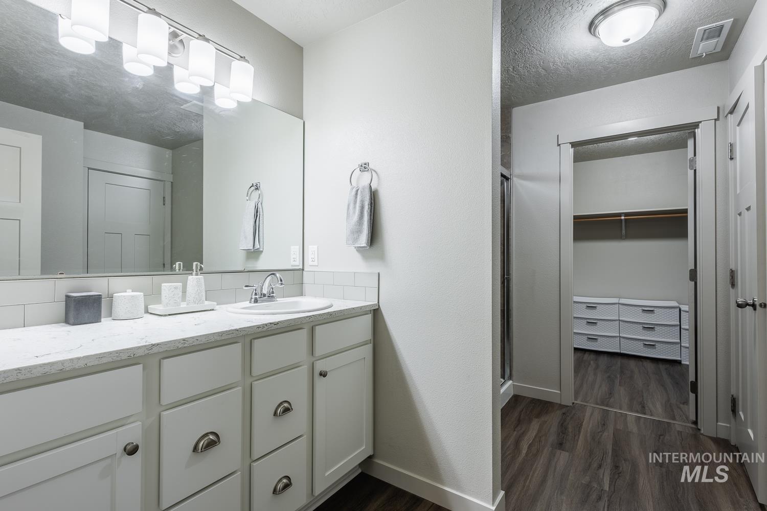 Bathroom featuring vanity, a textured ceiling, a shower stall, dark wood-style floors, and a walk in closet