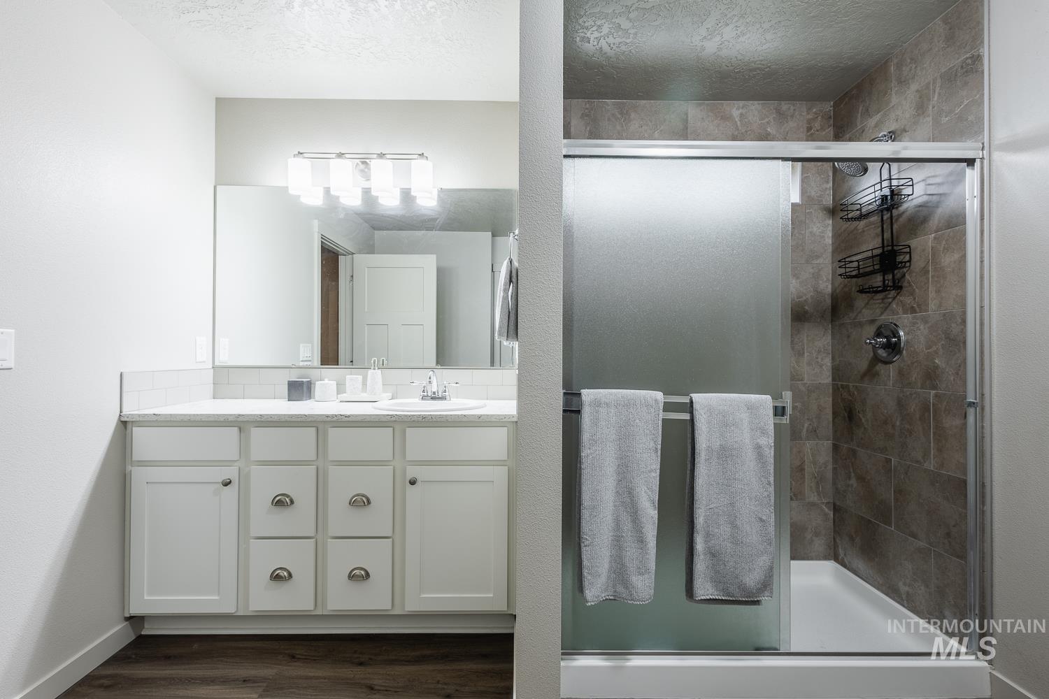 Full bath with a stall shower, vanity, dark wood-type flooring, and a textured ceiling