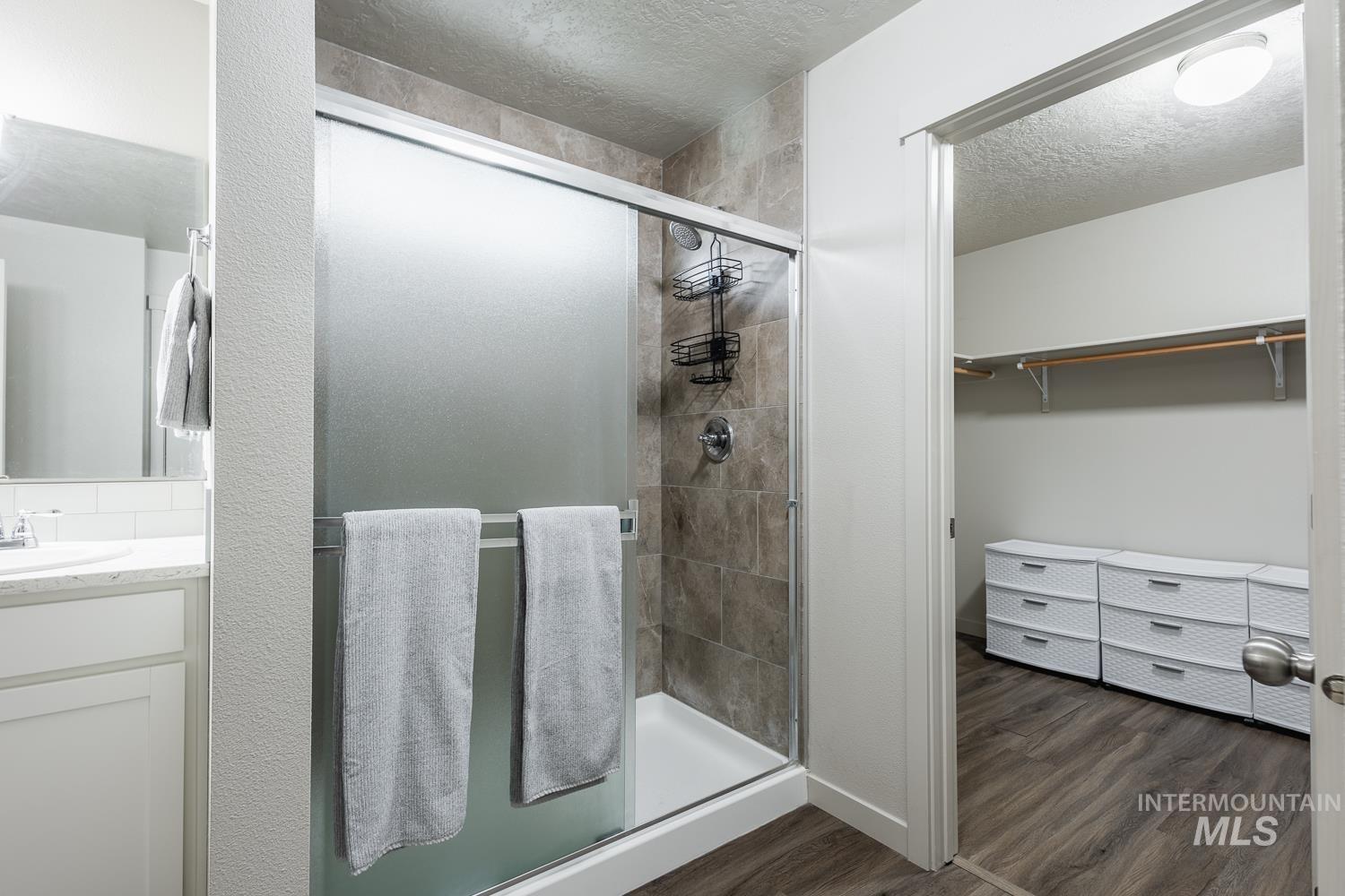 Bathroom with a stall shower, dark wood-style flooring, a spacious closet, a textured ceiling, and vanity