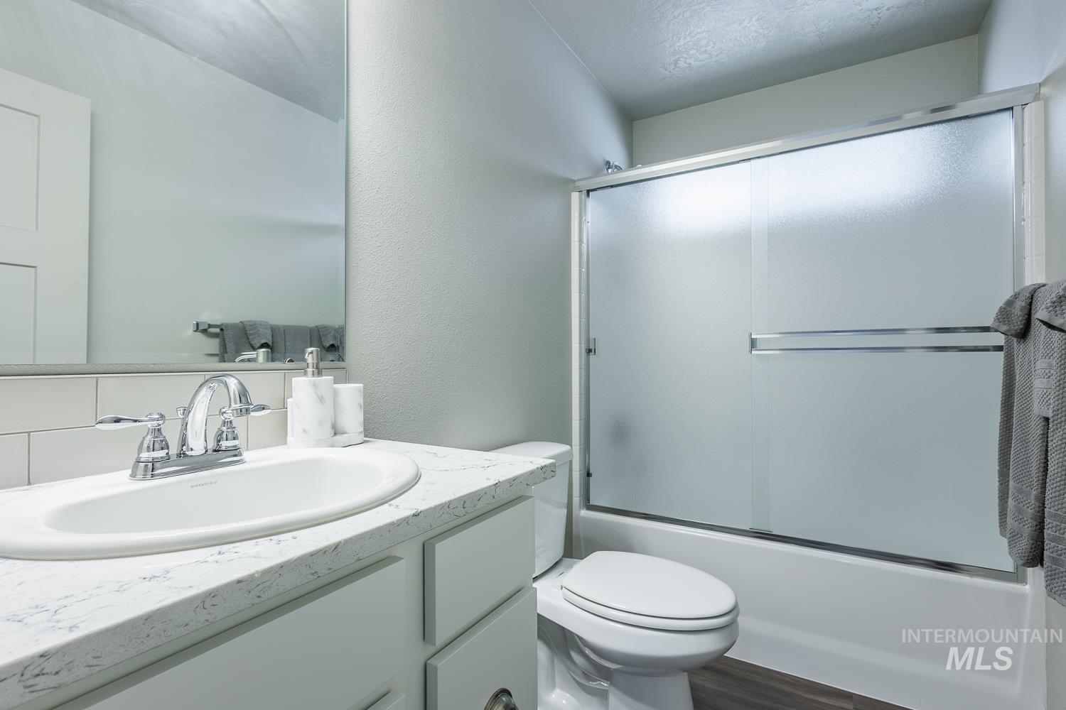 Bathroom with vanity, enclosed tub / shower combo, a textured wall, a textured ceiling, and dark wood-style floors