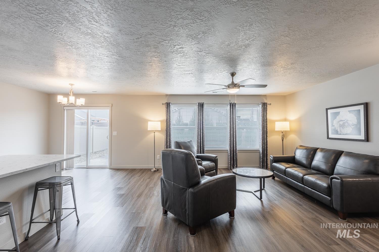 Living room featuring a textured ceiling, dark wood finished floors, ceiling fan, and a chandelier