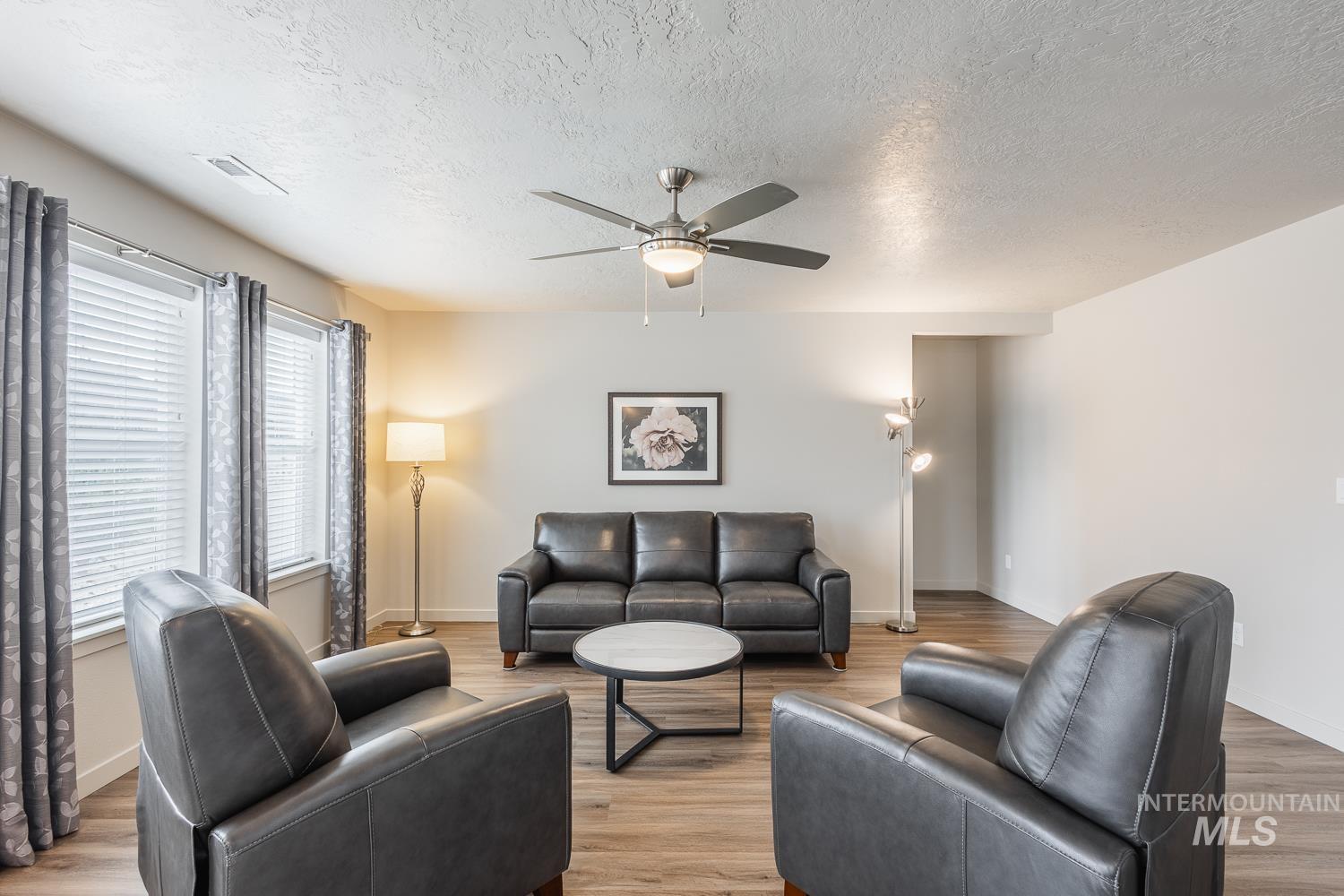 Living room with a textured ceiling, a ceiling fan, and light wood finished floors