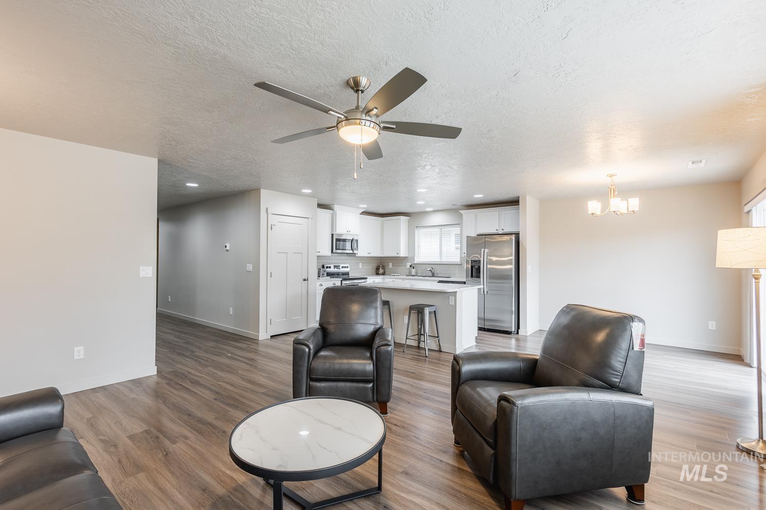 Living area with a textured ceiling, recessed lighting, light wood-style floors, ceiling fan, and a chandelier