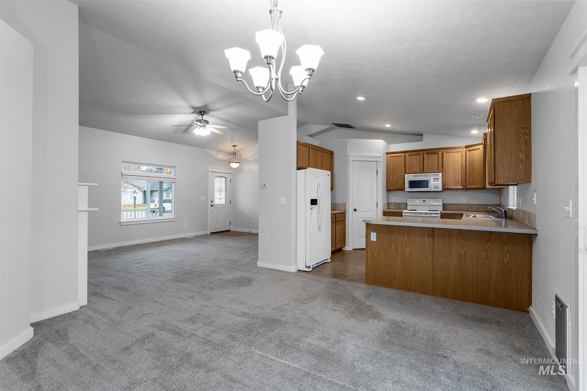 Kitchen with open floor plan, dark colored carpet, white appliances, a peninsula, and a chandelier