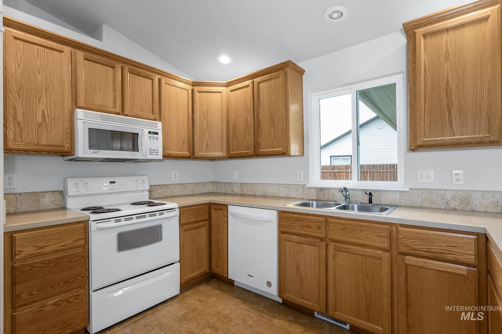 Kitchen with white appliances, light countertops, brown cabinets, recessed lighting, and lofted ceiling