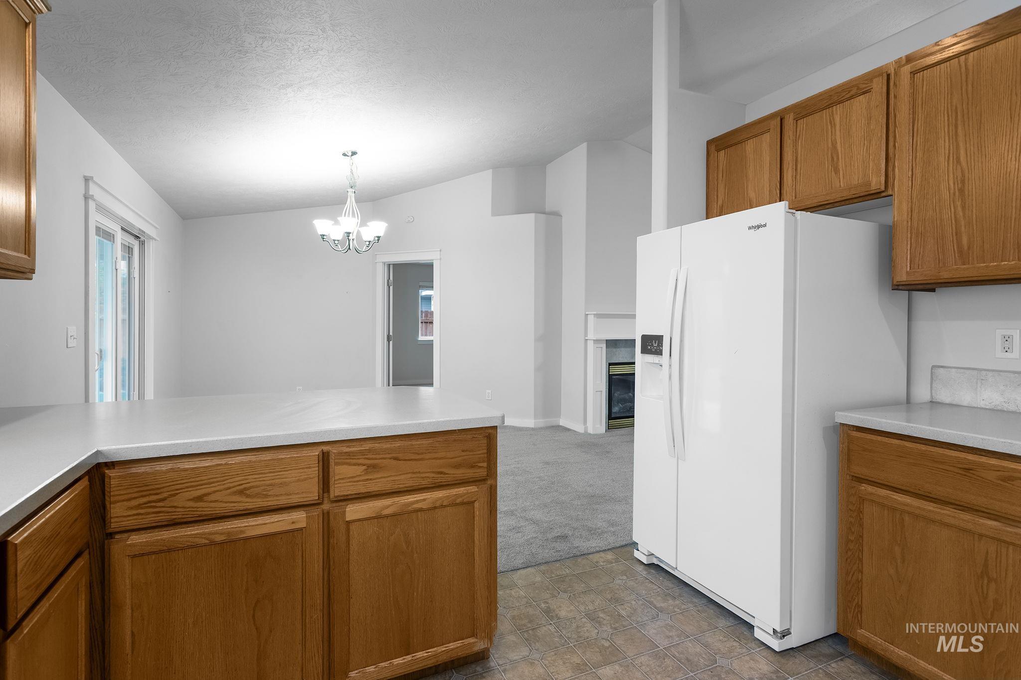 Kitchen with brown cabinetry, vaulted ceiling, white fridge with ice dispenser, a peninsula, and a chandelier