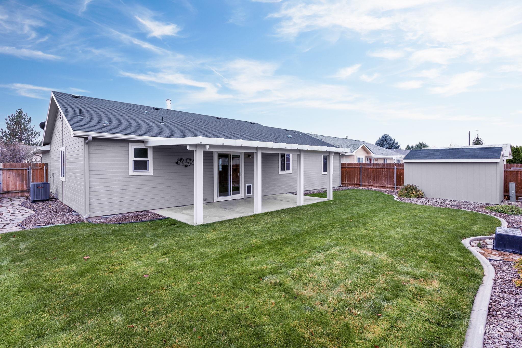 Rear view of property featuring a patio area, a shingled roof, a fenced backyard, and a storage shed