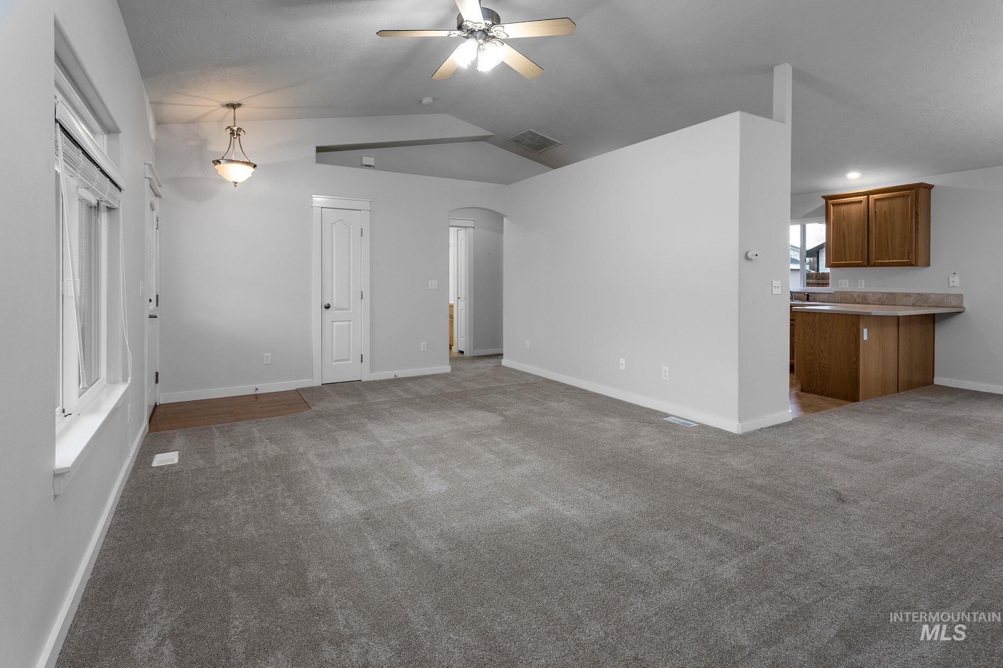 Unfurnished living room with arched walkways, carpet floors, lofted ceiling, and ceiling fan