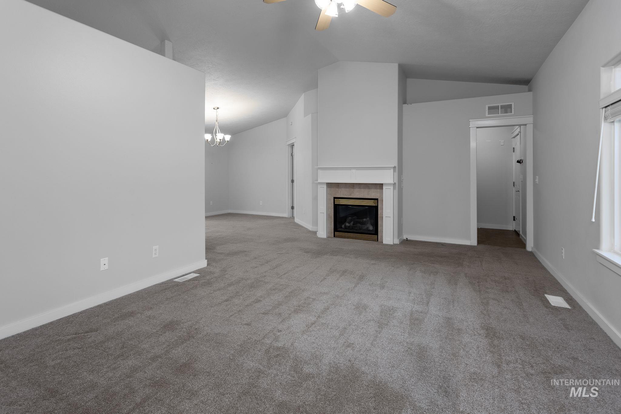 Unfurnished living room featuring lofted ceiling, carpet, a ceiling fan, a tile fireplace, and a chandelier