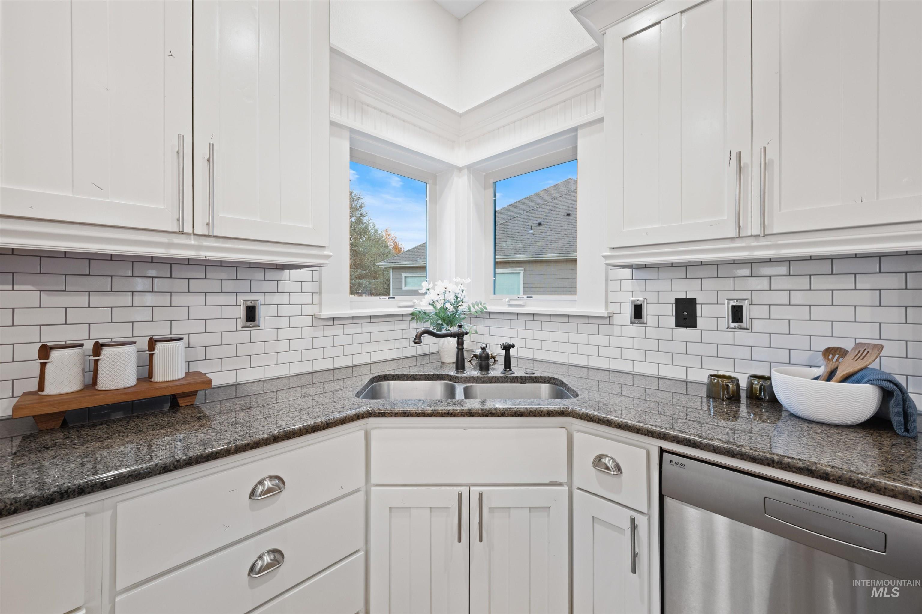 Kitchen featuring stainless steel dishwasher, white cabinetry, and dark stone countertops