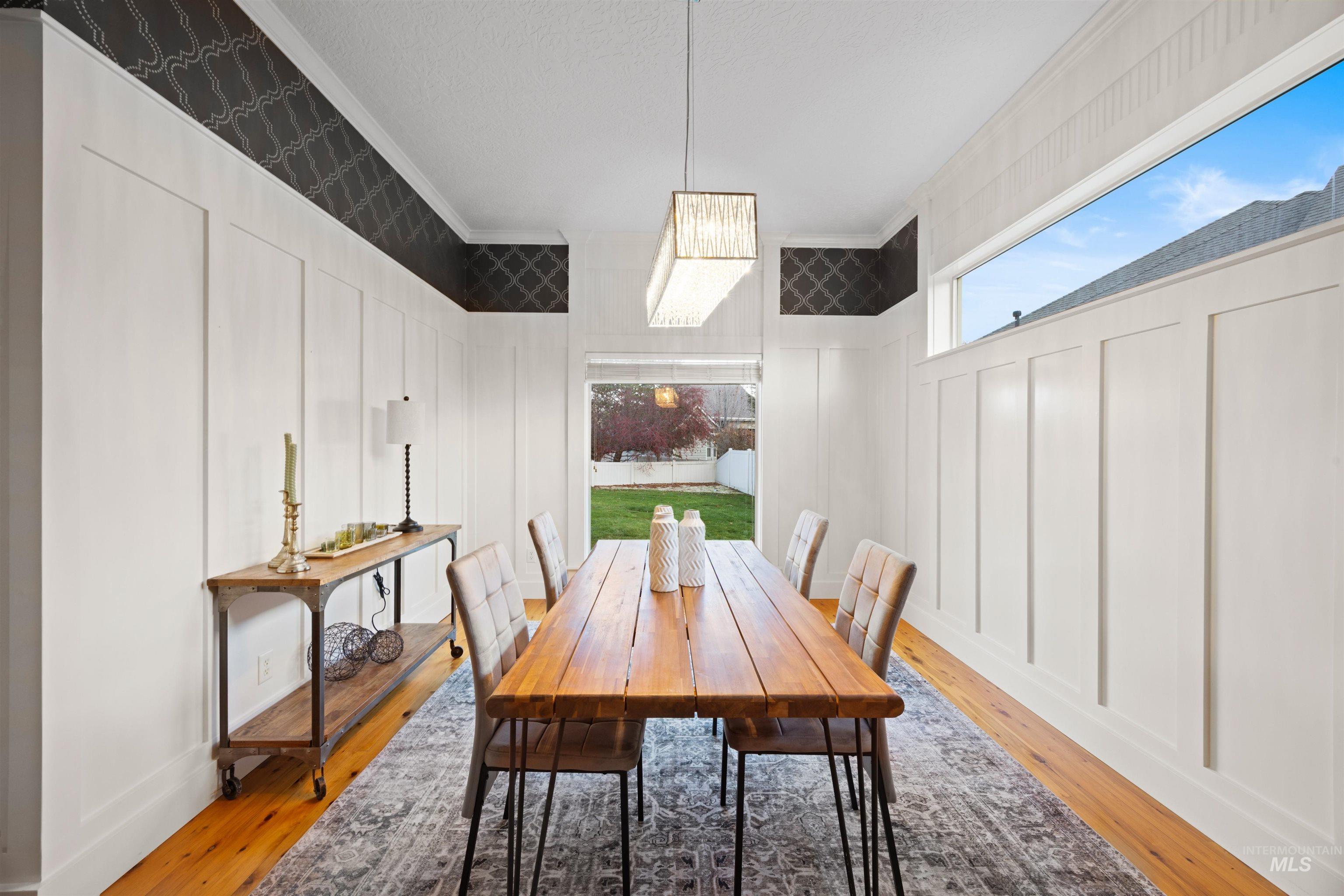 Dining space with ornamental molding, plenty of natural light, wood-type flooring, and a decorative wall