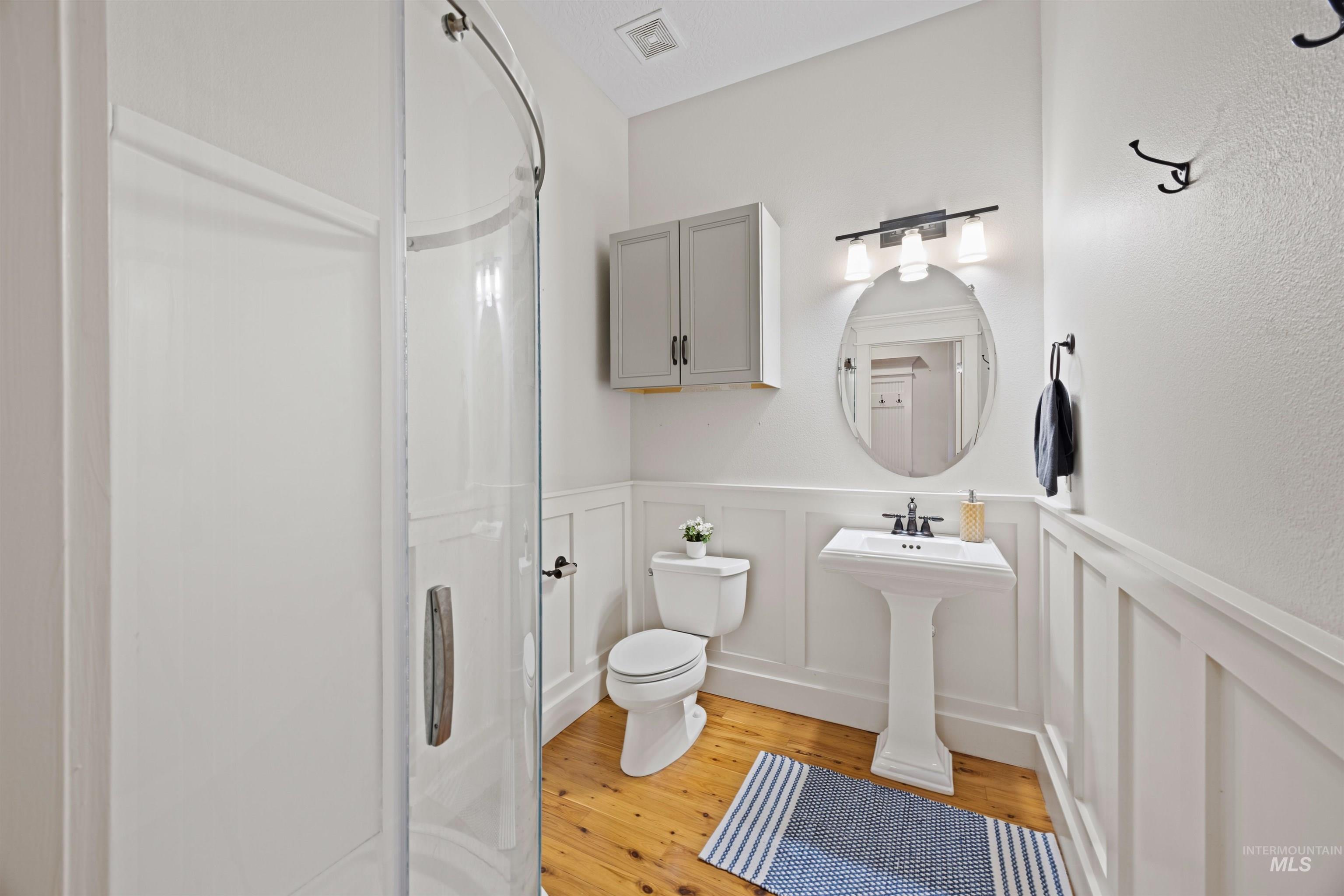 Full bath featuring a wainscoted wall, a decorative wall, light wood-style floors, and a shower stall