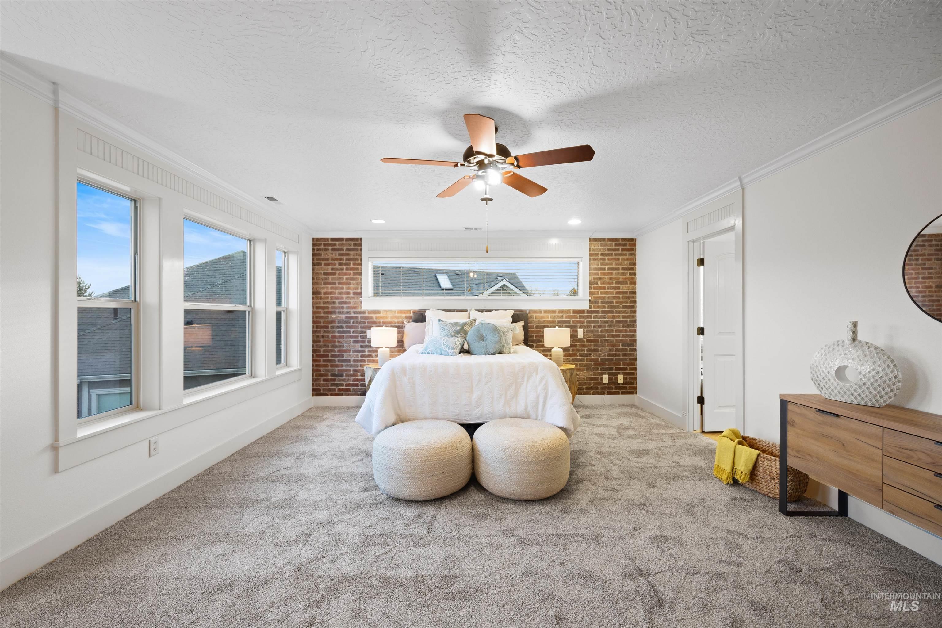 Bedroom with brick wall, crown molding, carpet, ceiling fan, and a textured ceiling