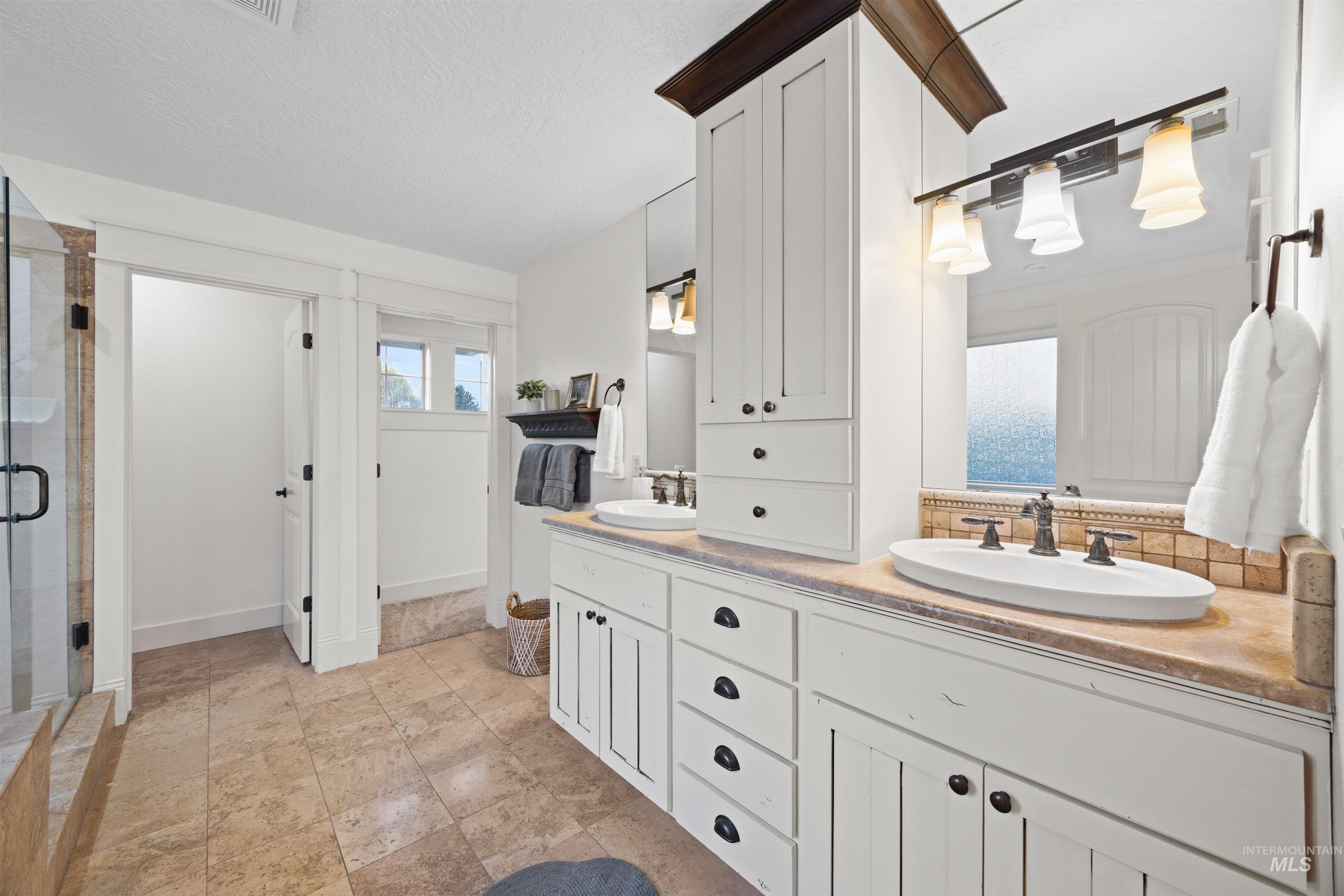 Full bathroom featuring double vanity, a shower stall, a textured ceiling, and backsplash