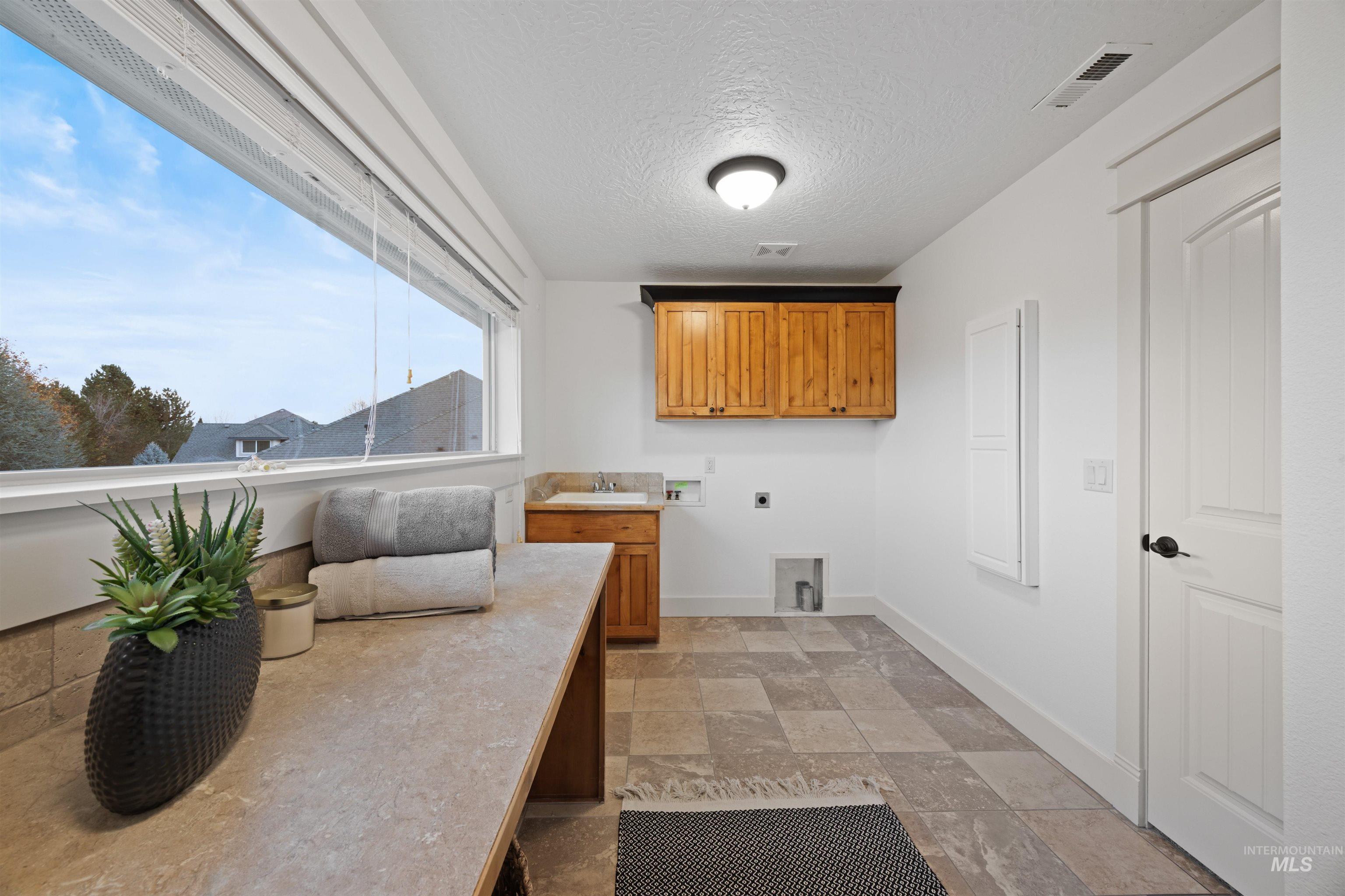 Laundry room featuring hookup for an electric dryer, washer hookup, stone tile flooring, a textured ceiling, and cabinet space