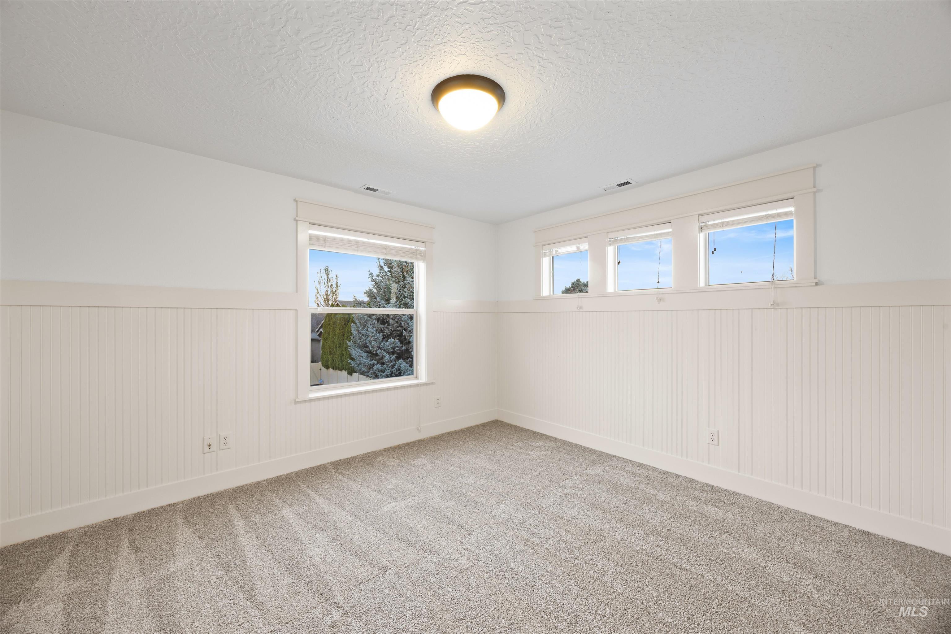 Carpeted spare room featuring a textured ceiling, wainscoting, and wooden walls