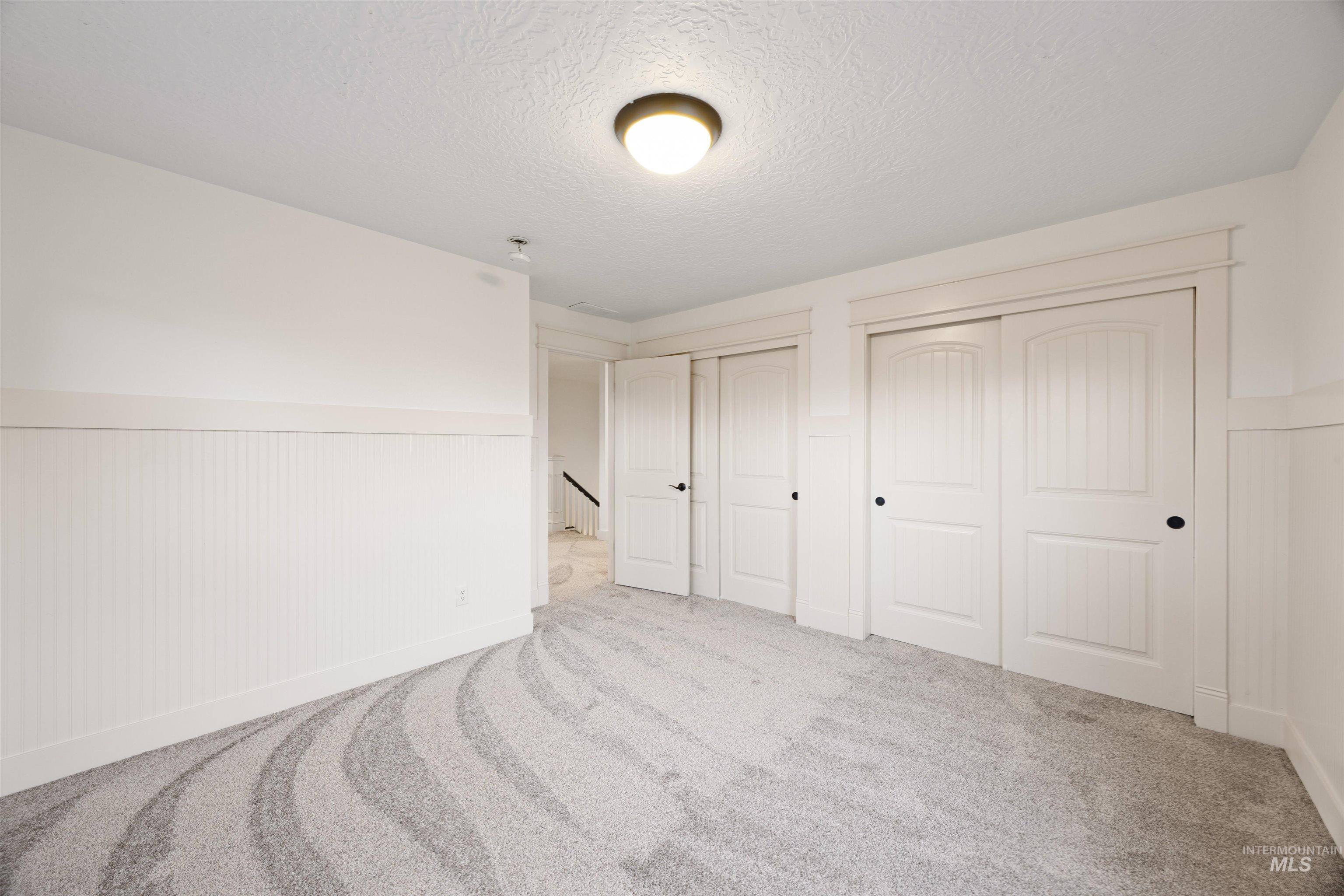Unfurnished bedroom with a wainscoted wall, two closets, light colored carpet, and a textured ceiling