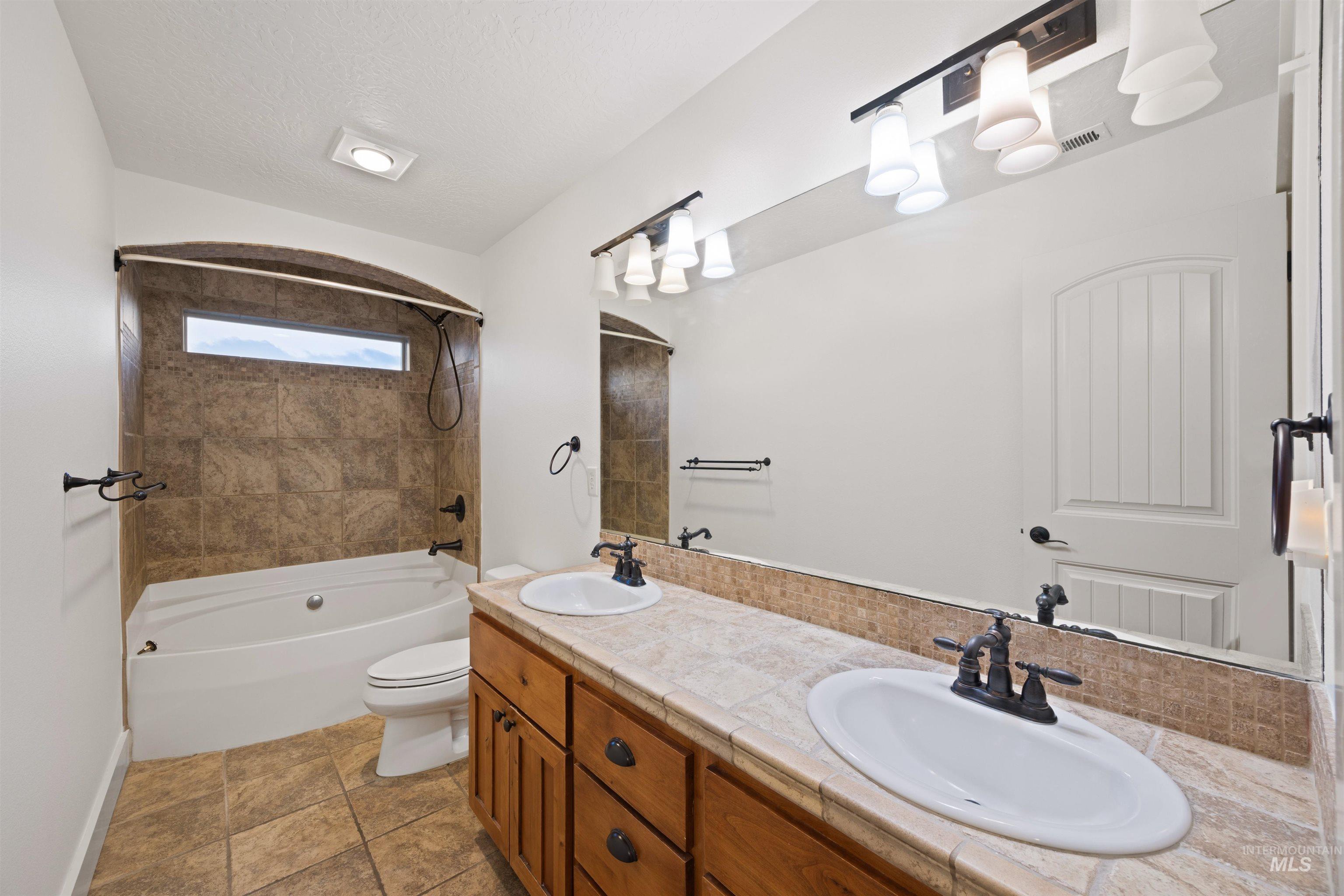 Bathroom with double vanity, bathing tub / shower combination, and a textured ceiling