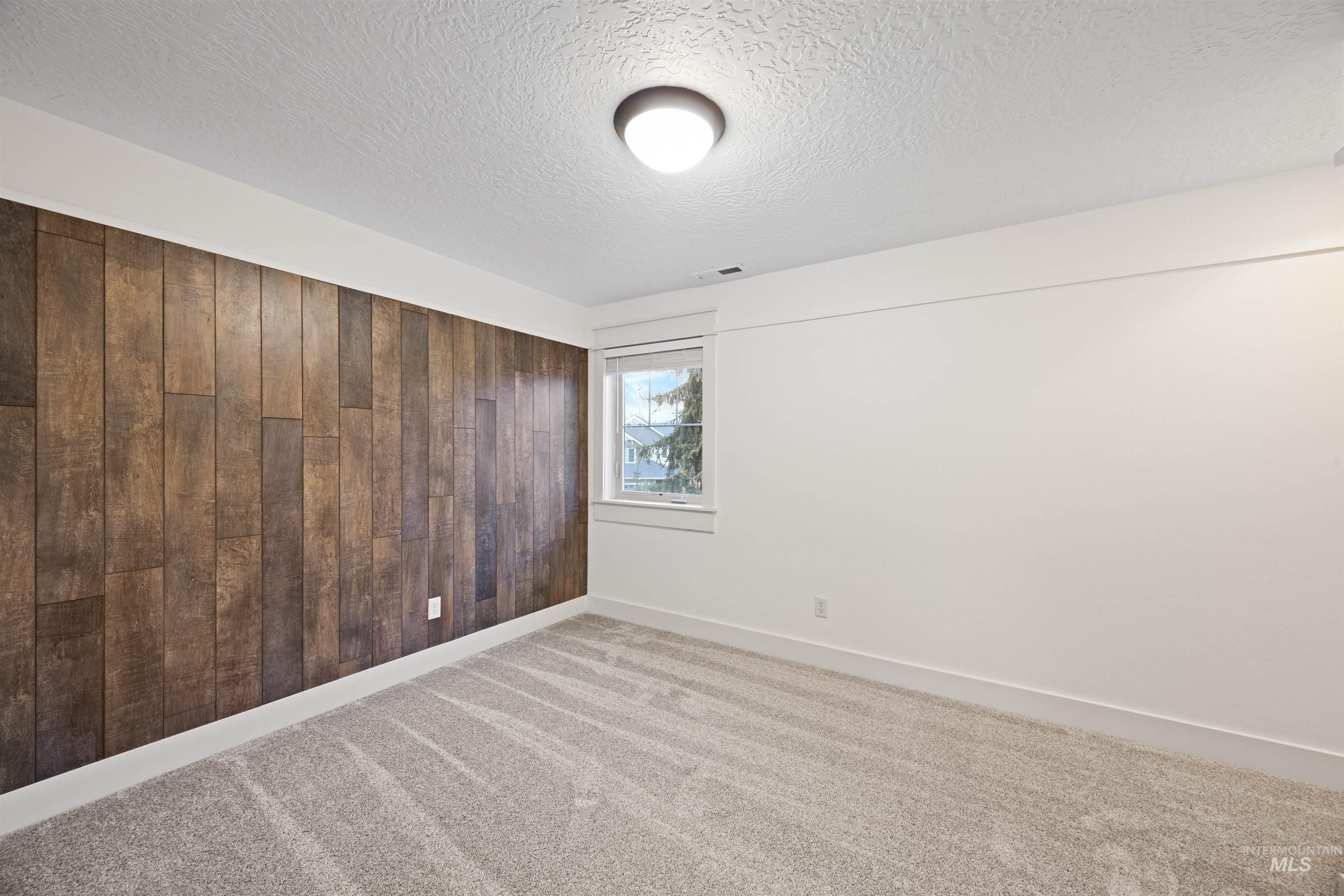 Carpeted spare room with wooden walls and a textured ceiling