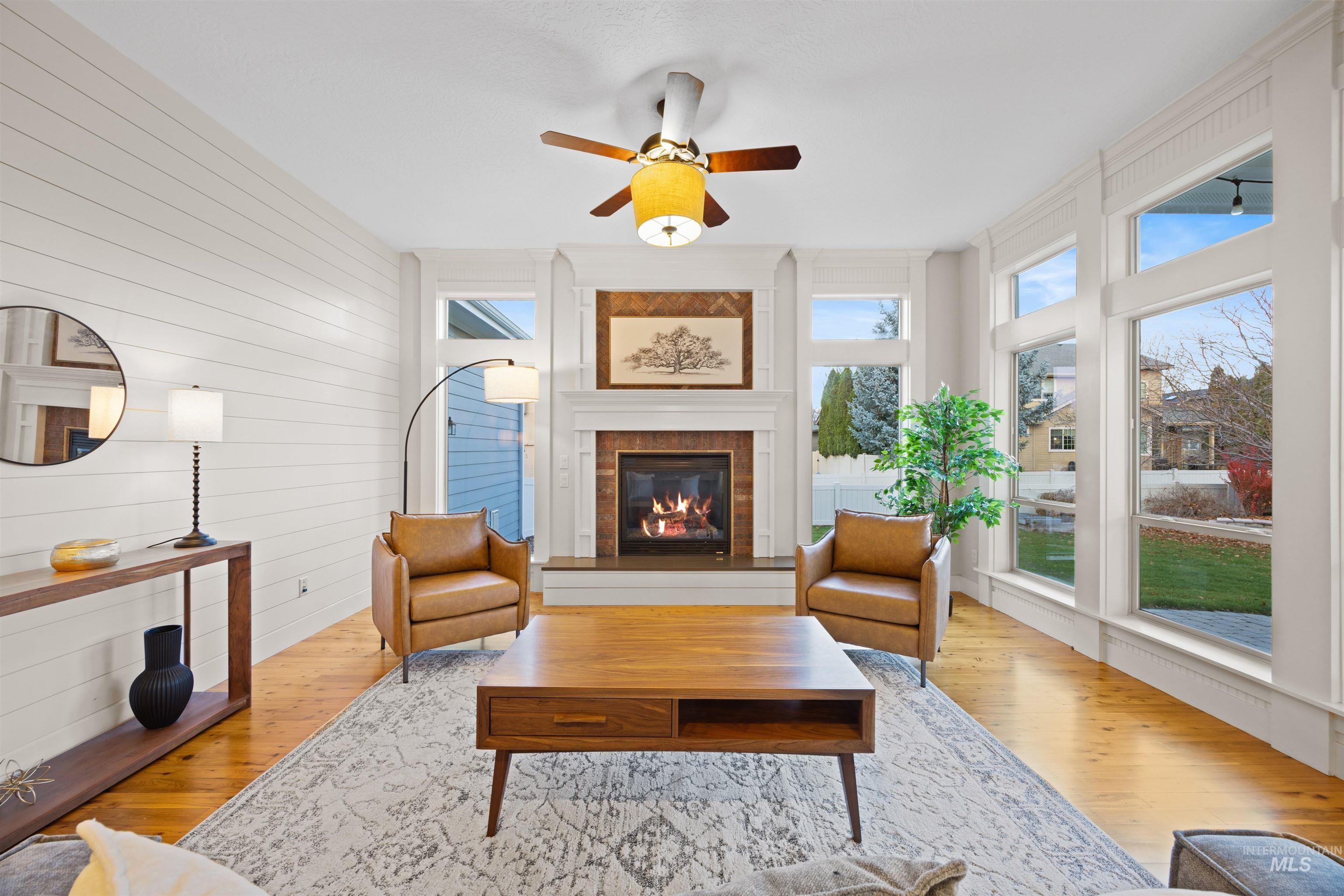 Living room with ceiling fan, wood finished floors, wooden walls, and a glass covered fireplace
